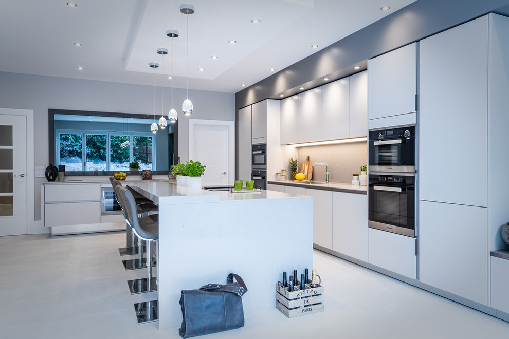 Large contemporary kitchen/diner in Hampshire with flat-panel cabinets, grey cabinets, engineered stone countertops, grey splashback, stone slab splashback, stainless steel appliances, an island and grey worktops.