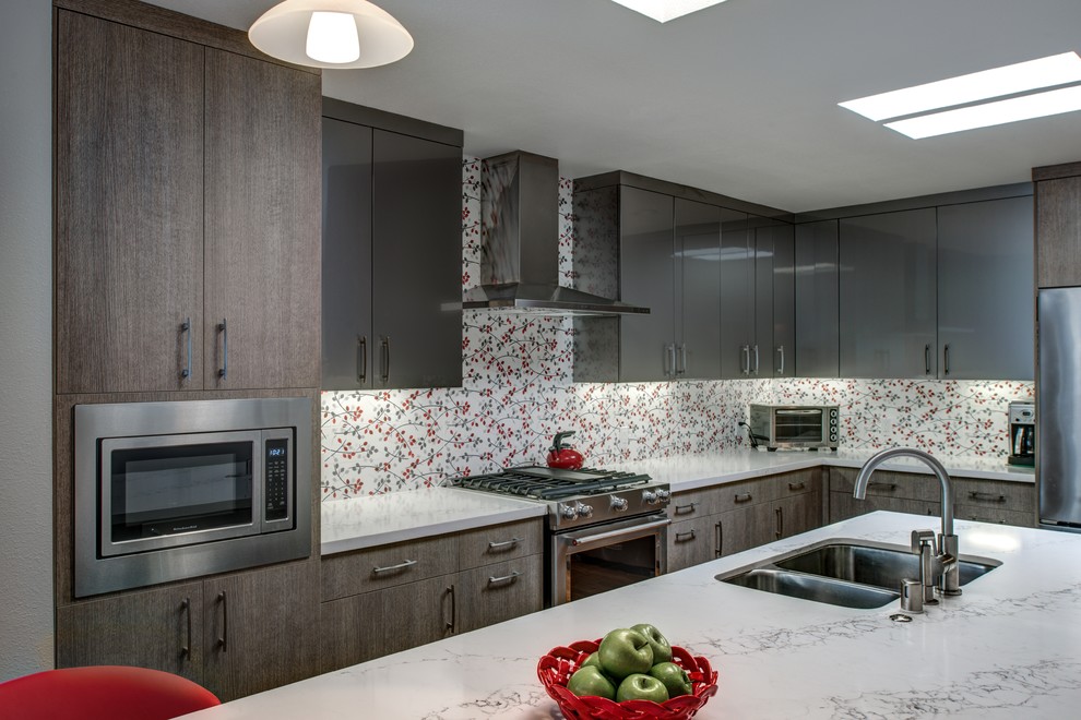 Bild på ett mellanstort funkis kök, med en undermonterad diskho, släta luckor, grå skåp, bänkskiva i kvarts, rött stänkskydd, stänkskydd i porslinskakel, rostfria vitvaror, mellanmörkt trägolv och en köksö