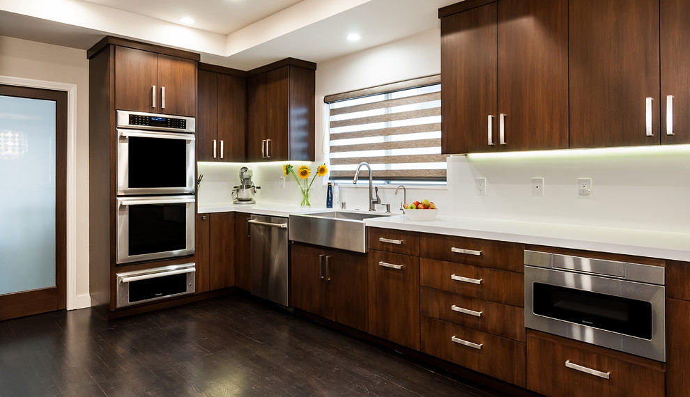 Enclosed kitchen - large modern galley dark wood floor and brown floor enclosed kitchen idea in Los Angeles with a farmhouse sink, flat-panel cabinets, dark wood cabinets, quartz countertops, white backsplash, stone slab backsplash, stainless steel appliances and no island
