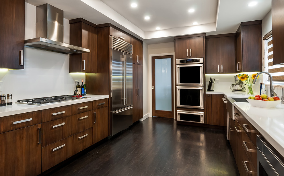 Inspiration for a large modern galley dark wood floor and brown floor enclosed kitchen remodel in Los Angeles with a farmhouse sink, flat-panel cabinets, dark wood cabinets, quartz countertops, white backsplash, stone slab backsplash, stainless steel appliances and no island