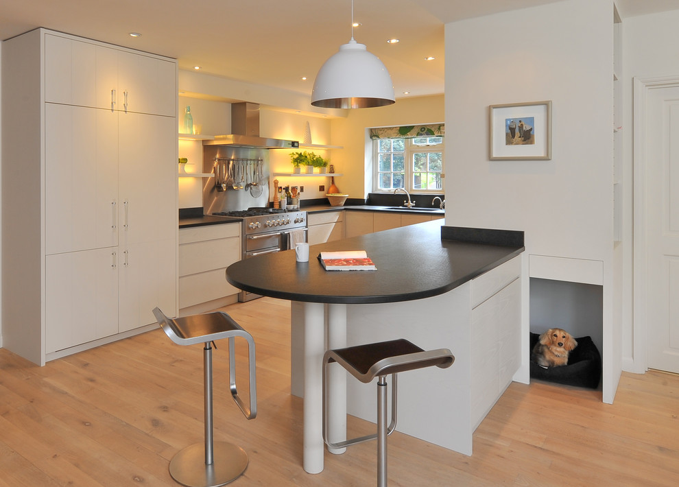 Example of a trendy u-shaped kitchen design in Hampshire with flat-panel cabinets and white cabinets