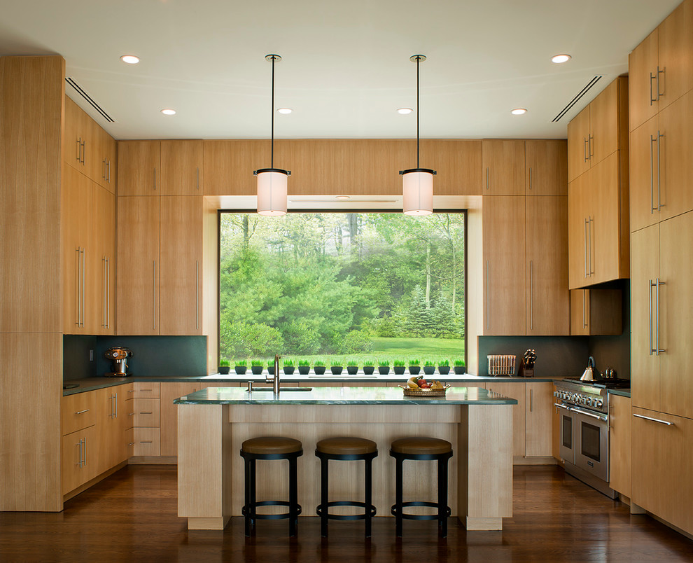 This is an example of a modern u-shaped kitchen in New York with flat-panel cabinets, light wood cabinets, green splashback, stainless steel appliances and green worktops.
