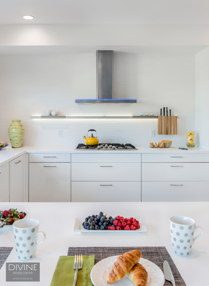 Photo of a medium sized contemporary u-shaped kitchen/diner in Boston with a submerged sink, flat-panel cabinets, white cabinets, composite countertops, white splashback, porcelain splashback, stainless steel appliances, light hardwood flooring, a breakfast bar and beige floors.