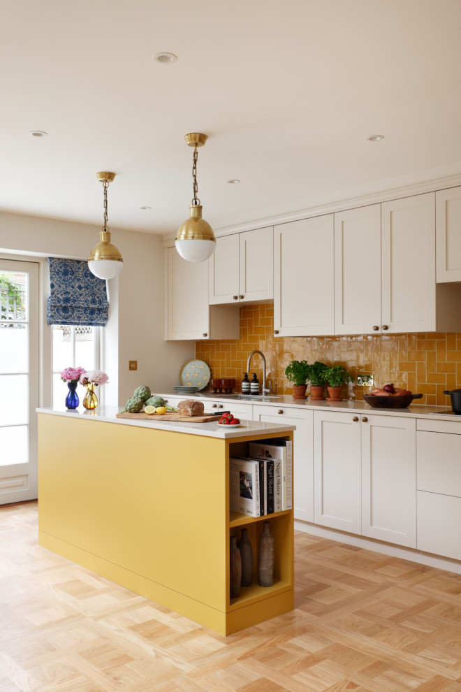 Classic galley kitchen in London with a submerged sink, shaker cabinets, white cabinets, orange splashback, light hardwood flooring, an island, beige floors and beige worktops.
