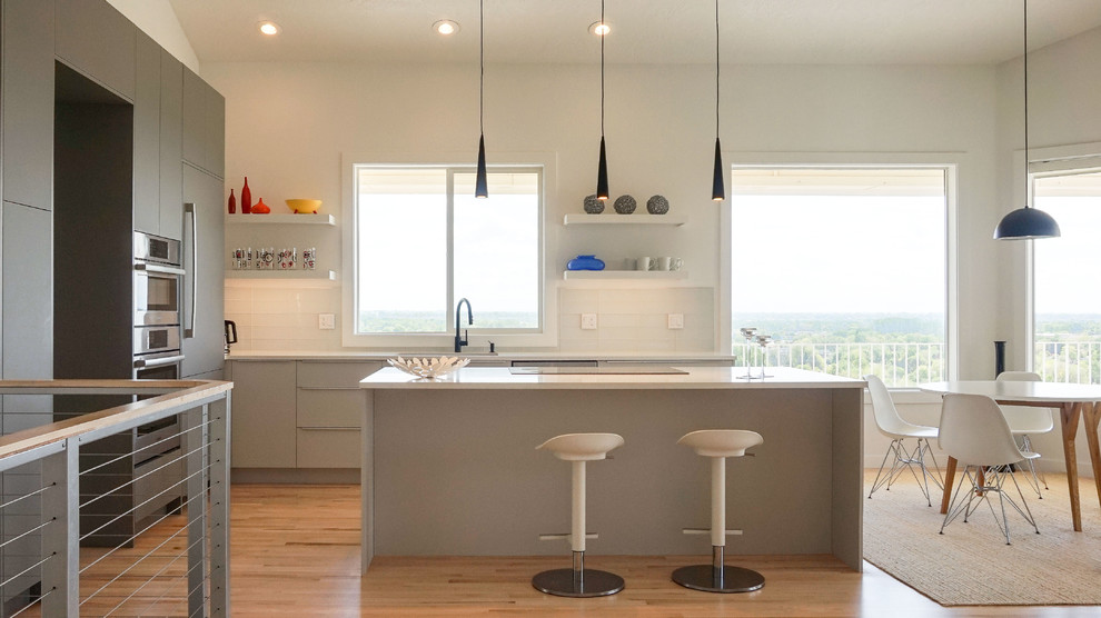 Modern inredning av ett mellanstort vit linjärt vitt kök med öppen planlösning, med en undermonterad diskho, släta luckor, grå skåp, bänkskiva i kvarts, grått stänkskydd, stänkskydd i glaskakel, färgglada vitvaror, ljust trägolv och en köksö