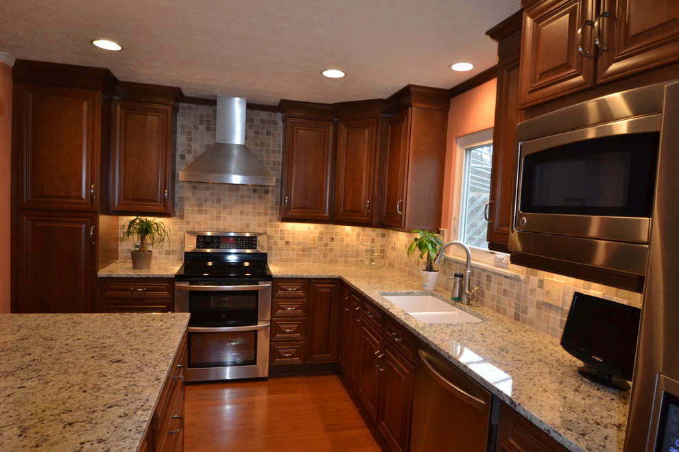 Example of a mid-sized transitional l-shaped medium tone wood floor eat-in kitchen design in Columbus with an undermount sink, raised-panel cabinets, dark wood cabinets, granite countertops, beige backsplash, stone tile backsplash, stainless steel appliances and an island