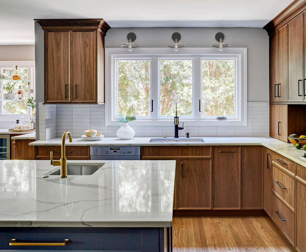Inspiration for a large classic l-shaped open plan kitchen in Chicago with a submerged sink, medium wood cabinets, white splashback, medium hardwood flooring, an island, brown floors, flat-panel cabinets, engineered stone countertops, metro tiled splashback, stainless steel appliances and white worktops.