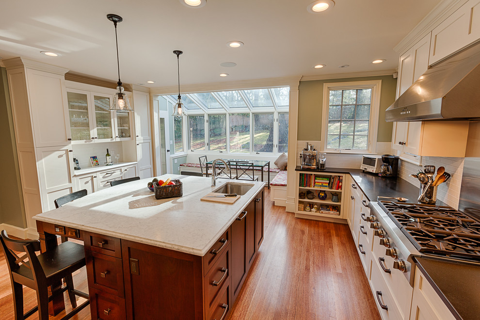 Mid-sized arts and crafts u-shaped medium tone wood floor eat-in kitchen photo in Boston with an undermount sink, shaker cabinets, white cabinets, marble countertops, white backsplash, stainless steel appliances and an island