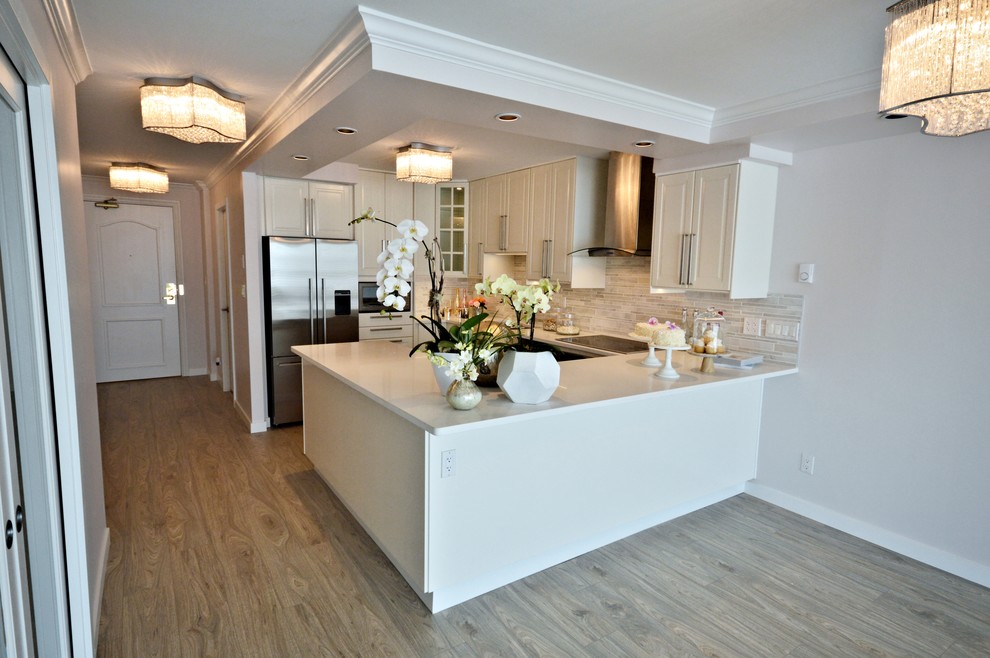 This is an example of a medium sized traditional u-shaped open plan kitchen in Vancouver with raised-panel cabinets, white cabinets, engineered stone countertops, a breakfast bar, white worktops, grey splashback, matchstick tiled splashback, stainless steel appliances, a double-bowl sink, medium hardwood flooring and brown floors.