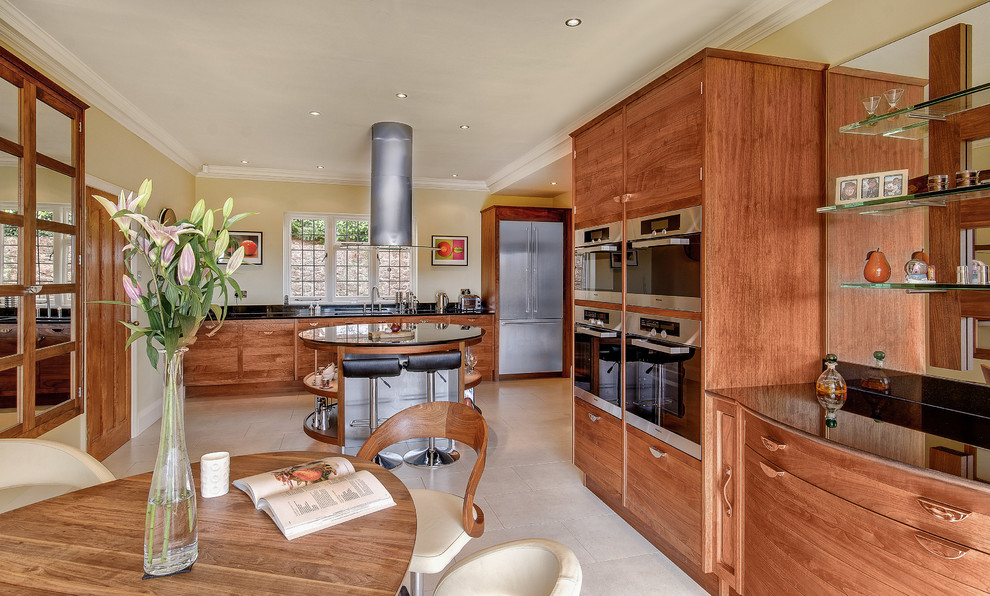 Cette image montre une grande cuisine design en L et bois brun avec un placard à porte plane, un plan de travail en granite, un électroménager en acier inoxydable et un sol en carrelage de céramique.
