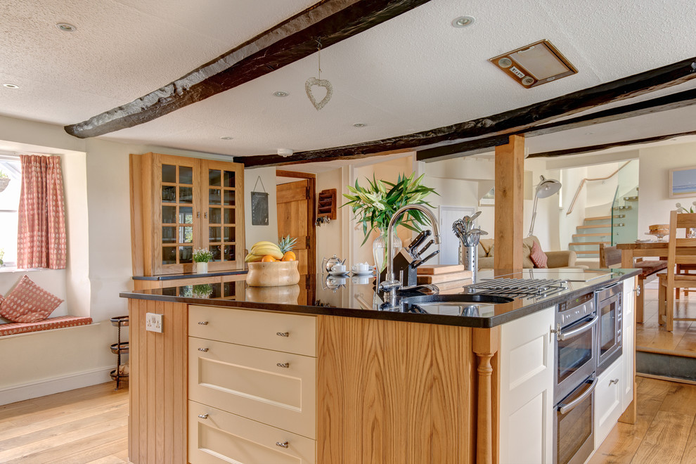 Große Landhausstil Wohnküche mit Schrankfronten mit vertiefter Füllung, hellbraunen Holzschränken, Granit-Arbeitsplatte, bunten Elektrogeräten, braunem Holzboden und Kücheninsel in Devon