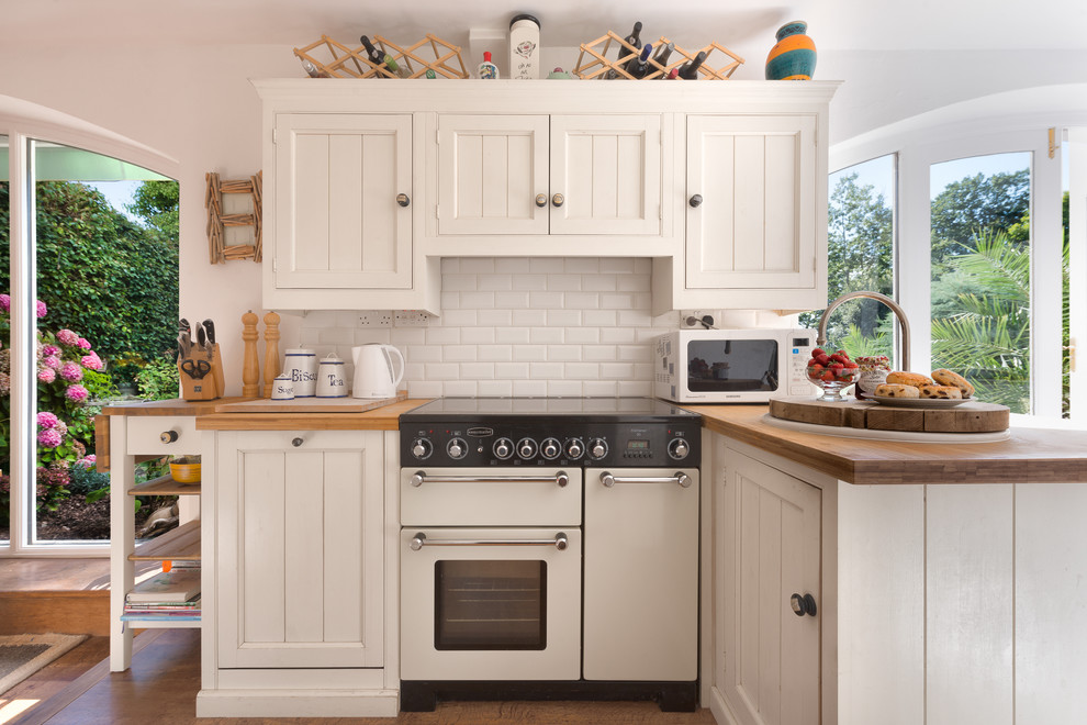 Inspiration for a small timeless l-shaped medium tone wood floor kitchen remodel in Devon with recessed-panel cabinets, white cabinets, wood countertops, white backsplash, white appliances, a peninsula and subway tile backsplash