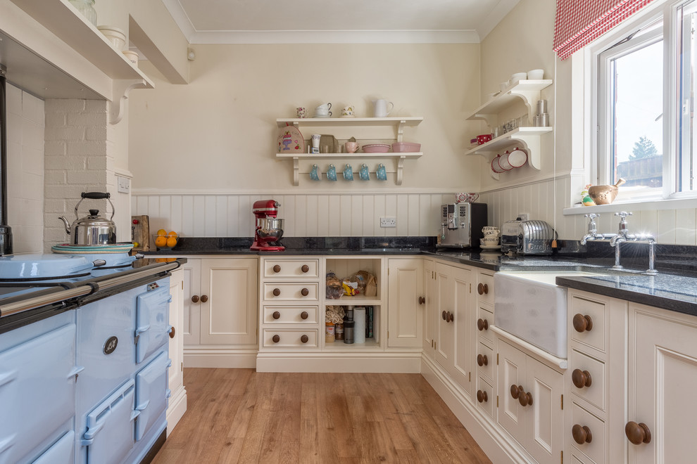 Photo of a large rural kitchen in Devon with a belfast sink, beaded cabinets, beige cabinets, coloured appliances, medium hardwood flooring and an island.