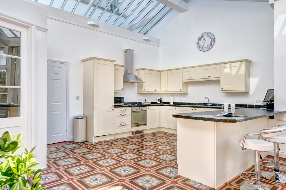 Geräumige Klassische Wohnküche in U-Form mit Schrankfronten mit vertiefter Füllung, beigen Schränken, Granit-Arbeitsplatte, Keramikboden und Halbinsel in Devon