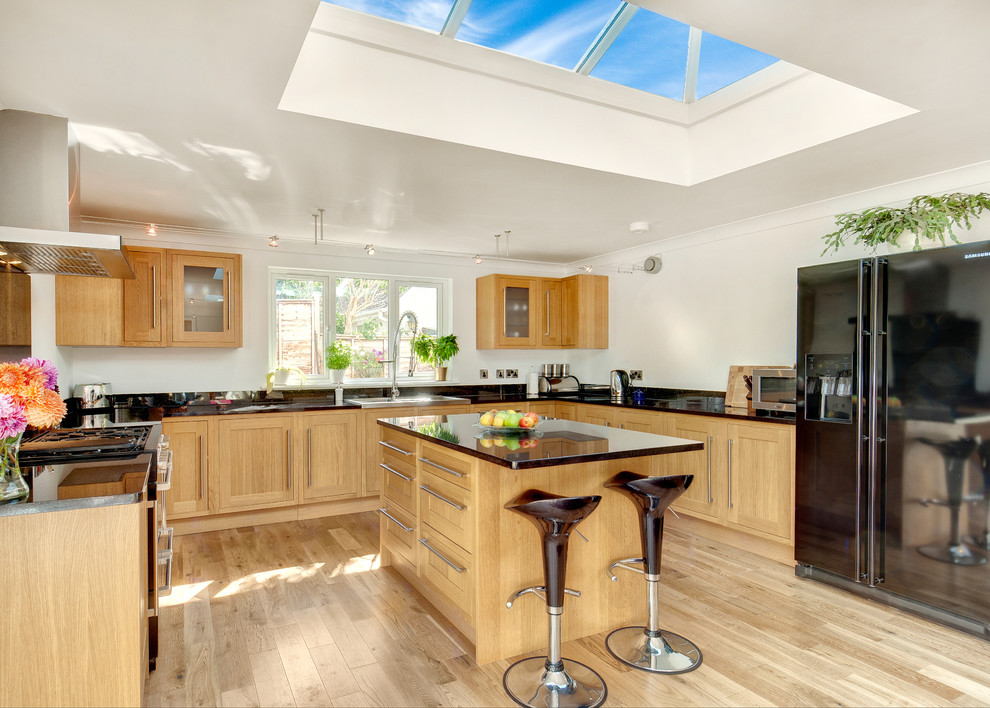 Design ideas for a large traditional u-shaped open plan kitchen in Devon with recessed-panel cabinets, medium wood cabinets, granite worktops, black appliances, medium hardwood flooring and an island.