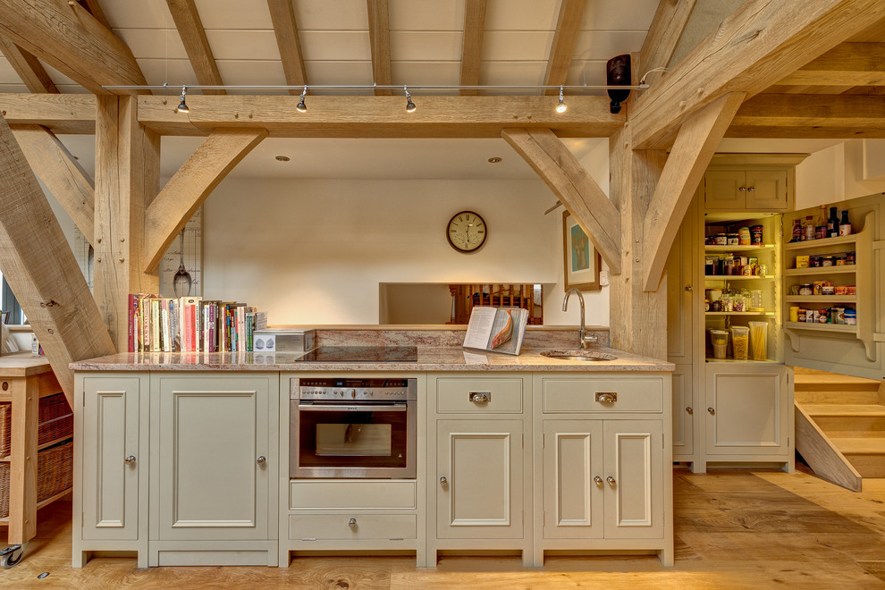 Geräumige Landhausstil Küche mit Kassettenfronten, beigen Schränken, Granit-Arbeitsplatte, Küchengeräten aus Edelstahl, braunem Holzboden und Kücheninsel in Devon