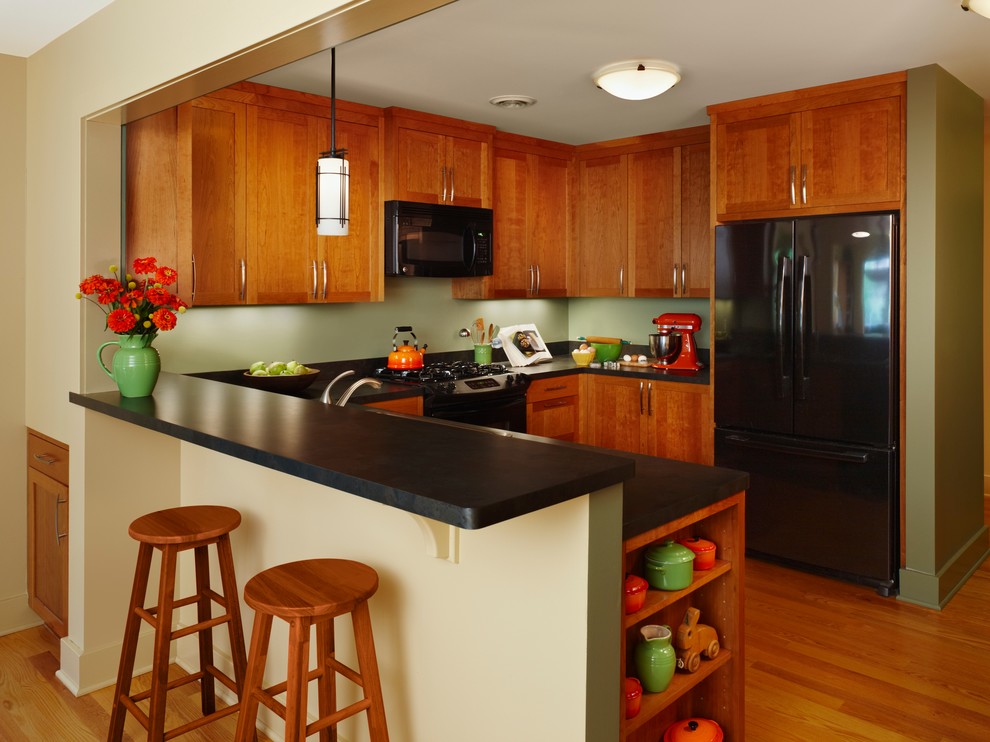 Foto de cocinas en U de estilo americano de tamaño medio abierto con puertas de armario de madera oscura, electrodomésticos negros, suelo de madera en tonos medios, armarios estilo shaker, península, suelo beige, encimeras negras y encimera de laminado