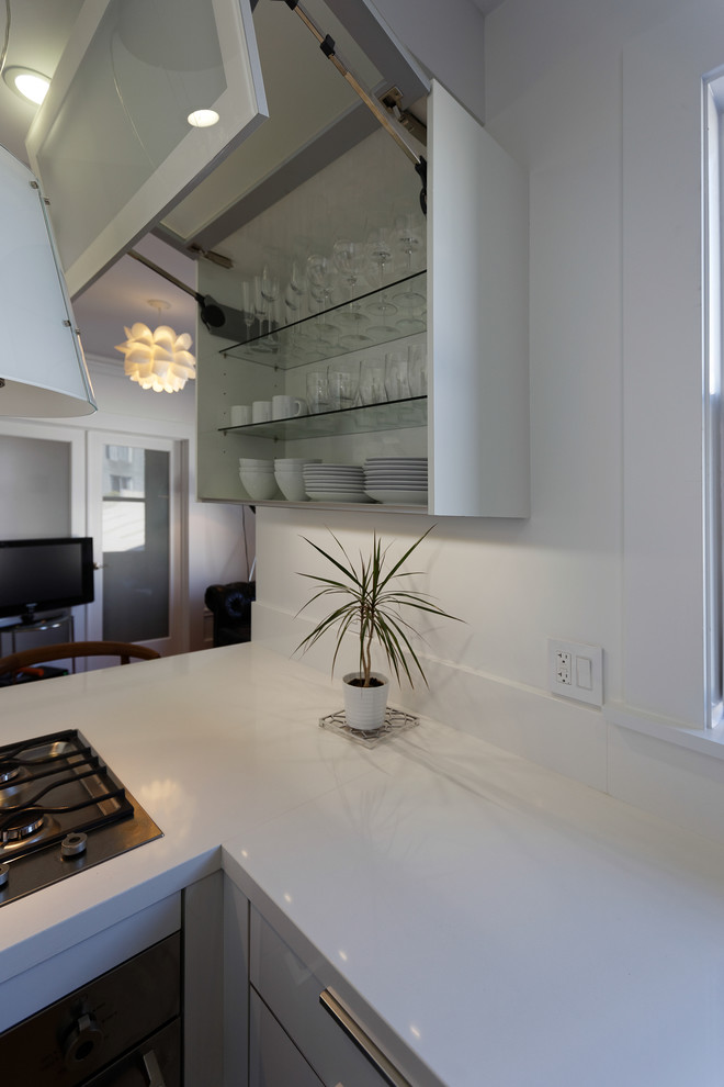 Small modern l-shaped open plan kitchen in San Francisco with a submerged sink, flat-panel cabinets, white cabinets, engineered stone countertops, white splashback, stainless steel appliances, medium hardwood flooring and no island.