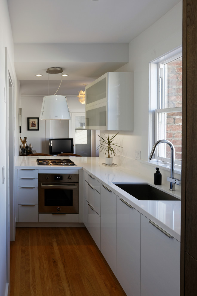 Foto på ett litet funkis kök, med en undermonterad diskho, släta luckor, vita skåp, bänkskiva i kvarts, vitt stänkskydd, rostfria vitvaror och mellanmörkt trägolv