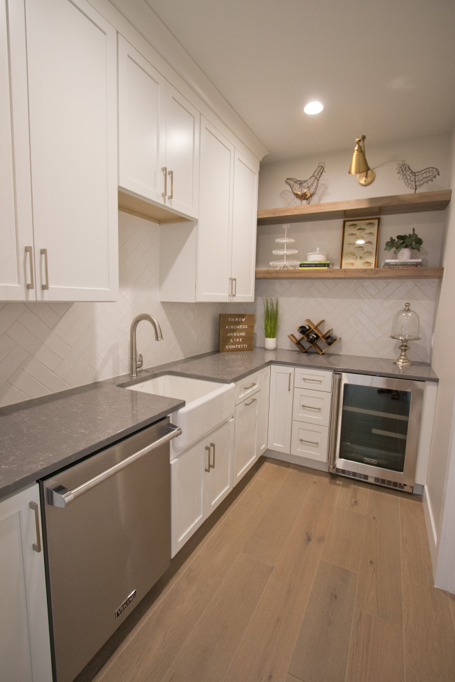 French country l-shaped light wood floor and brown floor kitchen pantry photo in Other with a farmhouse sink, recessed-panel cabinets, quartz countertops, white backsplash, ceramic backsplash, stainless steel appliances, white cabinets and gray countertops