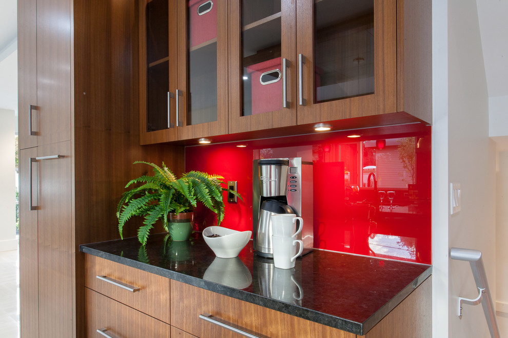 Modern inredning av ett stort kök, med en undermonterad diskho, släta luckor, skåp i mellenmörkt trä, granitbänkskiva, rött stänkskydd, stänkskydd i glaskakel, rostfria vitvaror, klinkergolv i porslin och en köksö