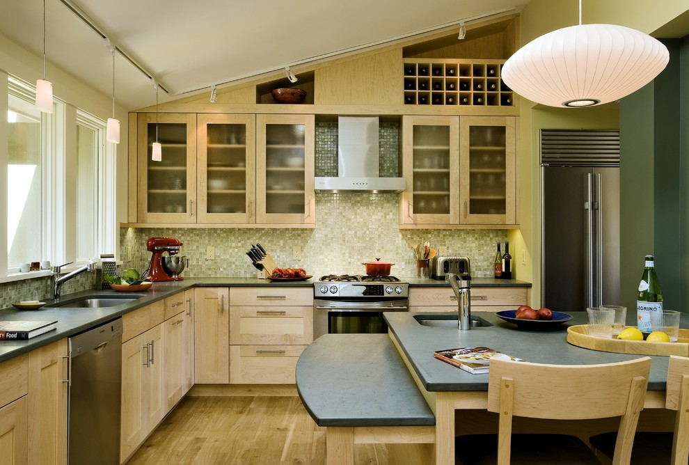 Inredning av ett modernt avskilt l-kök, med stänkskydd i mosaik, rostfria vitvaror, en undermonterad diskho, luckor med glaspanel, skåp i ljust trä och grönt stänkskydd