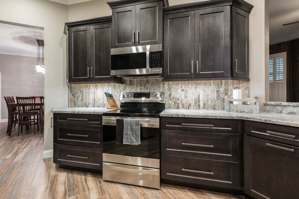 Example of a large transitional l-shaped porcelain tile and brown floor eat-in kitchen design in Orlando with shaker cabinets, gray cabinets, granite countertops, multicolored backsplash, travertine backsplash, stainless steel appliances, a peninsula and multicolored countertops