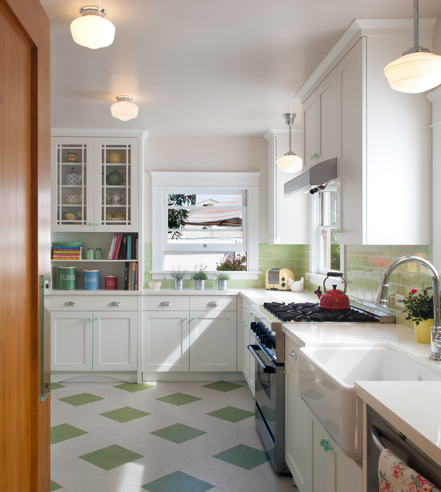 Photo of a medium sized traditional l-shaped kitchen/diner in San Diego with a belfast sink, recessed-panel cabinets, white cabinets, composite countertops, green splashback, glass tiled splashback, stainless steel appliances, lino flooring, no island, green floors and white worktops.