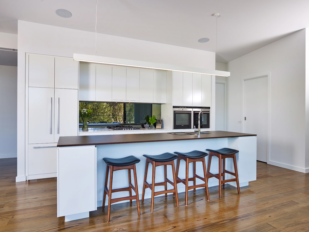 Inspiration for a large contemporary galley light wood floor and brown floor kitchen pantry remodel in Other with a drop-in sink, flat-panel cabinets, white cabinets, solid surface countertops, metallic backsplash, mirror backsplash, black appliances, an island and brown countertops