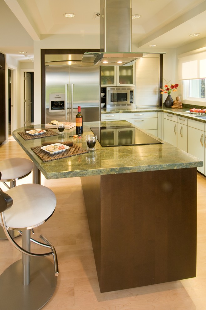 Пример оригинального дизайна: угловая кухня в современном стиле с стеклянными фасадами, техникой из нержавеющей стали, обеденным столом, врезной мойкой, гранитной столешницей, зеленым фартуком, зеленой столешницей и барной стойкой