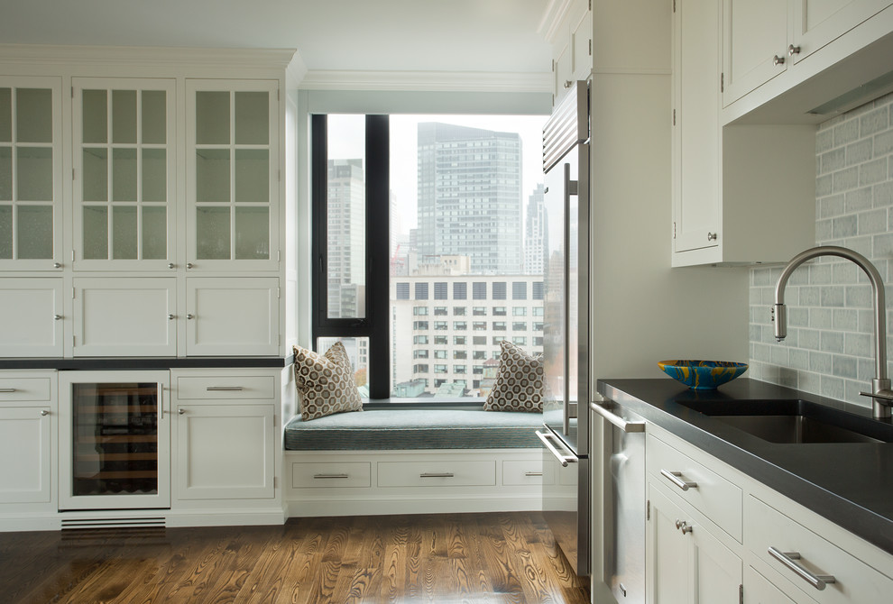 Inredning av ett klassiskt litet kök, med en undermonterad diskho, luckor med infälld panel, vita skåp, grått stänkskydd, stänkskydd i tunnelbanekakel, rostfria vitvaror och en köksö