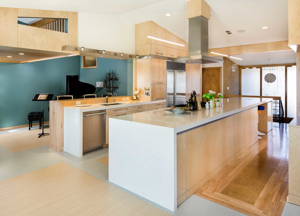 Imagen de cocina comedor actual grande con armarios con paneles lisos, puertas de armario de madera clara, electrodomésticos de acero inoxidable y una isla