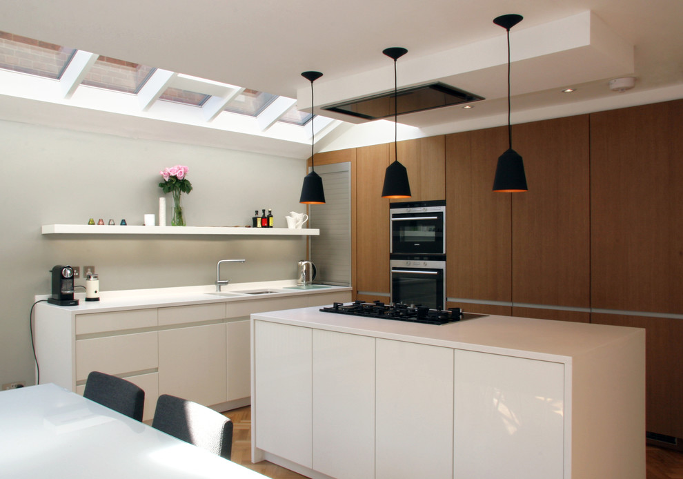 オックスフォードシャーにあるコンテンポラリースタイルのおしゃれなアイランドキッチン (ダブルシンク、フラットパネル扉のキャビネット、中間色木目調キャビネット、シルバーの調理設備) の写真