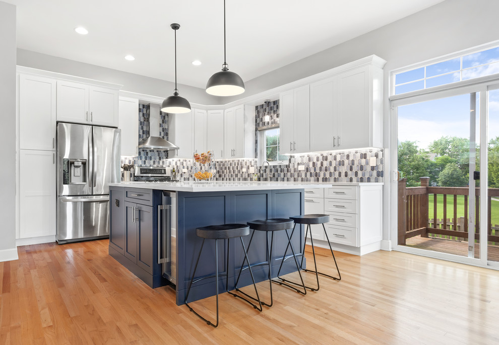 Mid-sized trendy l-shaped medium tone wood floor eat-in kitchen photo in Chicago with an undermount sink, shaker cabinets, white cabinets, quartz countertops, multicolored backsplash, mosaic tile backsplash, stainless steel appliances, an island and white countertops