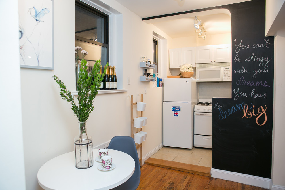 Einzeilige, Kleine Shabby-Look Wohnküche mit weißen Schränken und braunem Holzboden in New York