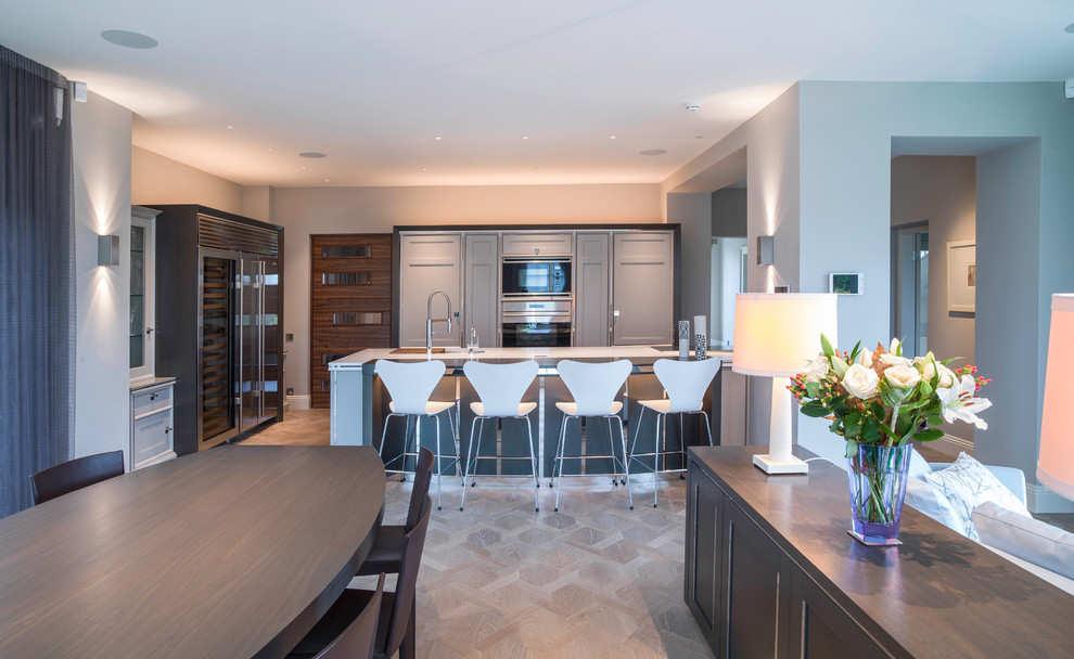 Photo of a large contemporary open plan kitchen in Hampshire with a submerged sink, beaded cabinets, grey cabinets, engineered stone countertops, stainless steel appliances, light hardwood flooring and an island.