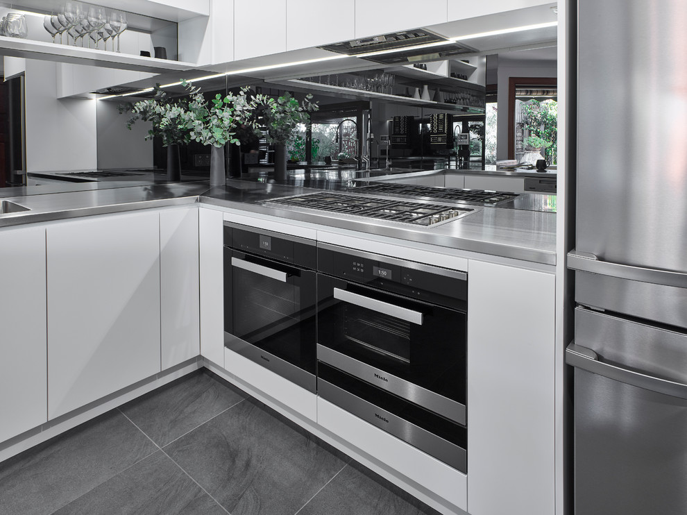 Large modern u-shaped kitchen/diner in Other with an integrated sink, white cabinets, stainless steel worktops, glass sheet splashback, stainless steel appliances, ceramic flooring and a breakfast bar.
