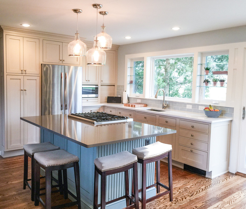 Klassisk inredning av ett mellanstort vit vitt l-kök, med en undermonterad diskho, skåp i shakerstil, beige skåp, blått stänkskydd, stänkskydd i keramik, rostfria vitvaror, mellanmörkt trägolv, en köksö och brunt golv