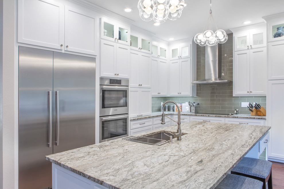 Große Klassische Wohnküche in L-Form mit Unterbauwaschbecken, Schrankfronten im Shaker-Stil, weißen Schränken, Granit-Arbeitsplatte, Küchenrückwand in Beige, Rückwand aus Glasfliesen, Küchengeräten aus Edelstahl, dunklem Holzboden, Kücheninsel, braunem Boden und beiger Arbeitsplatte in Sonstige