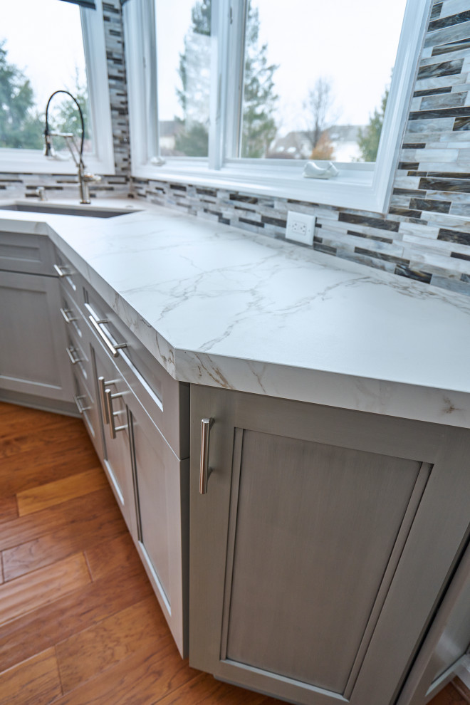 Inredning av ett klassiskt mellanstort vit vitt kök, med släta luckor, grå skåp, bänkskiva i kvarts, grått stänkskydd, stänkskydd i glaskakel, rostfria vitvaror och en köksö