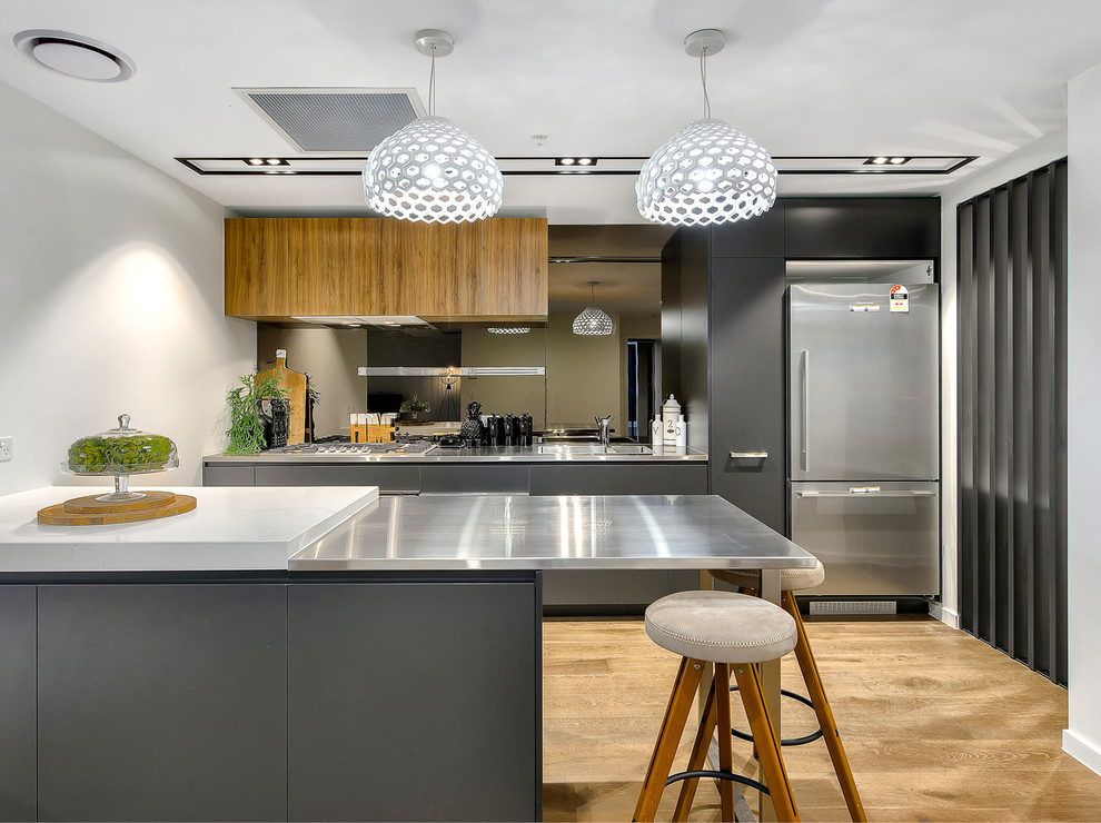 Einzeilige, Mittelgroße Moderne Küche in grau-weiß mit Doppelwaschbecken, flächenbündigen Schrankfronten, Edelstahl-Arbeitsplatte, Rückwand aus Spiegelfliesen, Küchengeräten aus Edelstahl, braunem Holzboden, Kücheninsel, braunem Boden und grauen Schränken in Brisbane