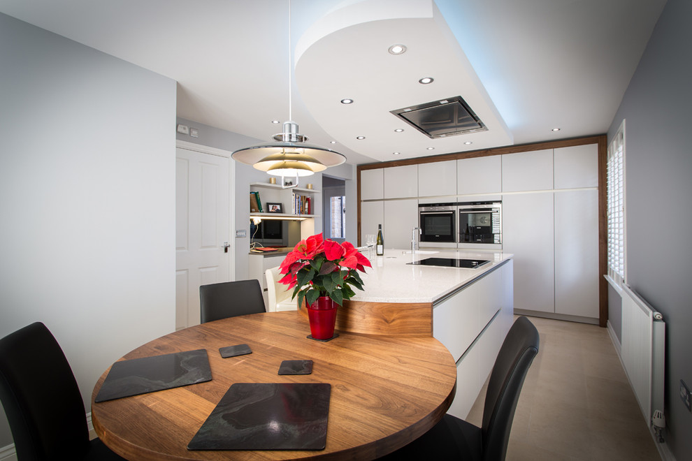 This is an example of a medium sized contemporary u-shaped kitchen/diner in Hampshire with flat-panel cabinets, white cabinets, composite countertops, metallic splashback, mirror splashback, stainless steel appliances and an island.