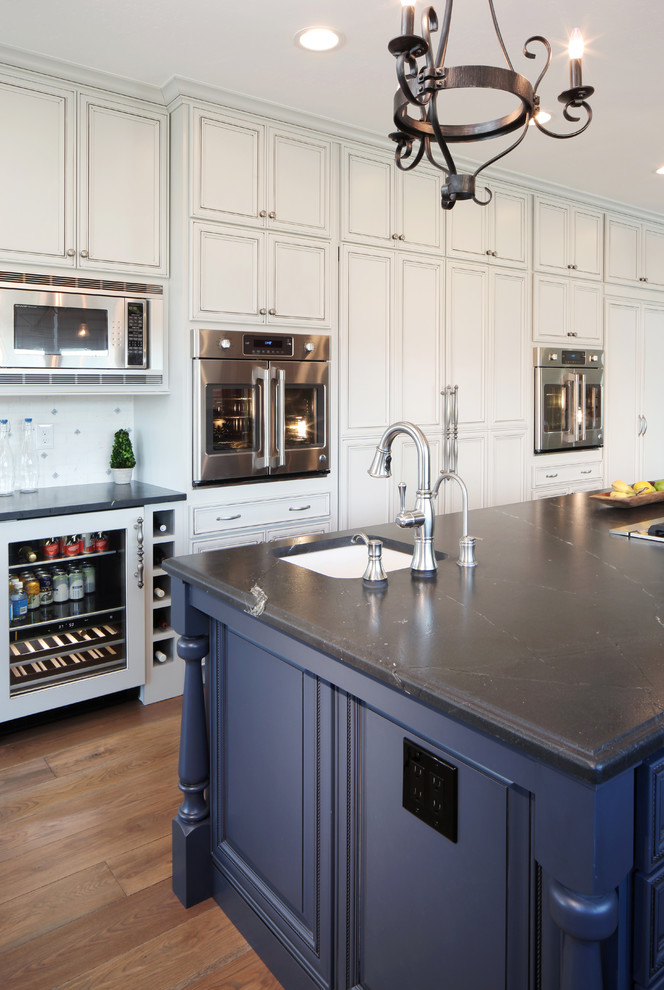 Example of a large classic medium tone wood floor kitchen design in Denver with recessed-panel cabinets, blue cabinets, granite countertops, white backsplash, ceramic backsplash, stainless steel appliances and an island