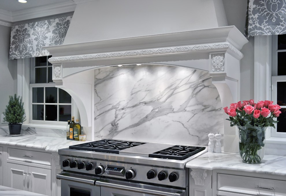 Example of a large classic l-shaped medium tone wood floor eat-in kitchen design in New York with an integrated sink, recessed-panel cabinets, white cabinets, marble countertops, white backsplash, stone slab backsplash, stainless steel appliances and an island