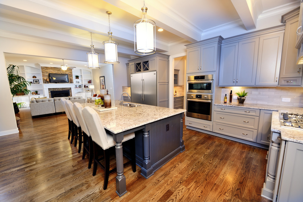 Klassisk inredning av ett kök, med grå skåp, granitbänkskiva, beige stänkskydd, rostfria vitvaror, mellanmörkt trägolv och en köksö