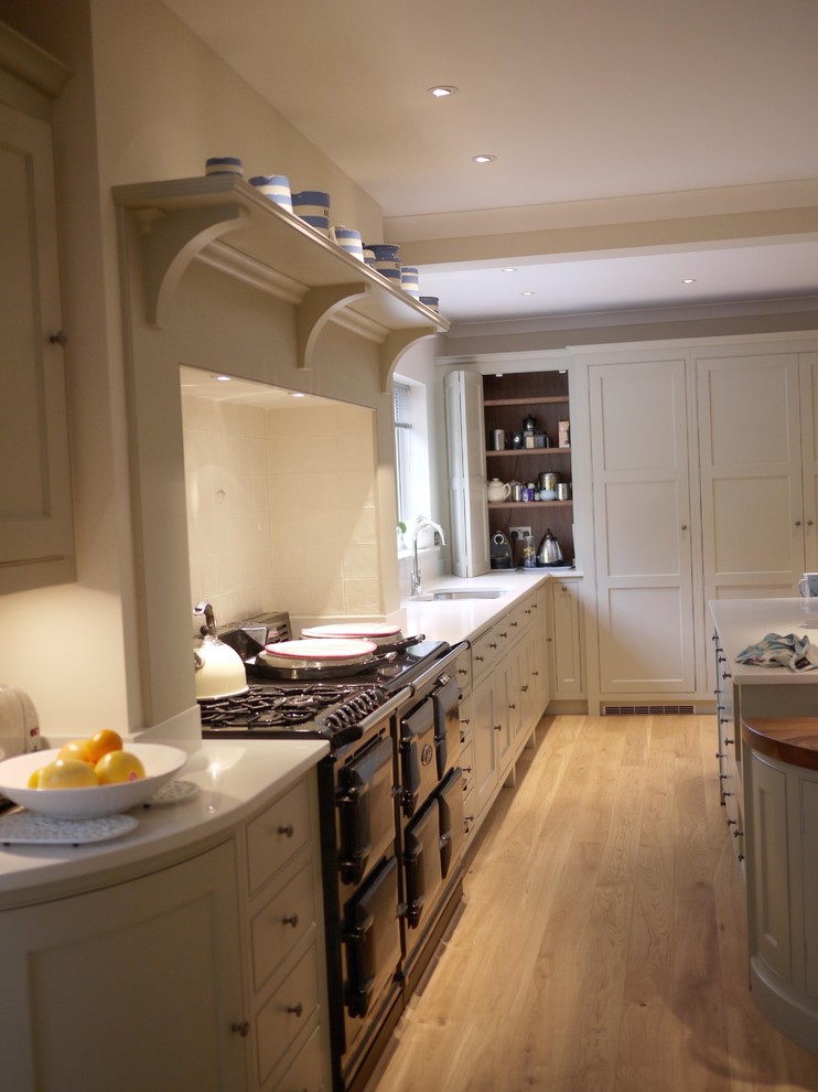 Photo of a large classic grey and cream u-shaped kitchen/diner in Hampshire with an integrated sink, recessed-panel cabinets, white cabinets, engineered stone countertops, beige splashback, ceramic splashback, black appliances, light hardwood flooring and an island.