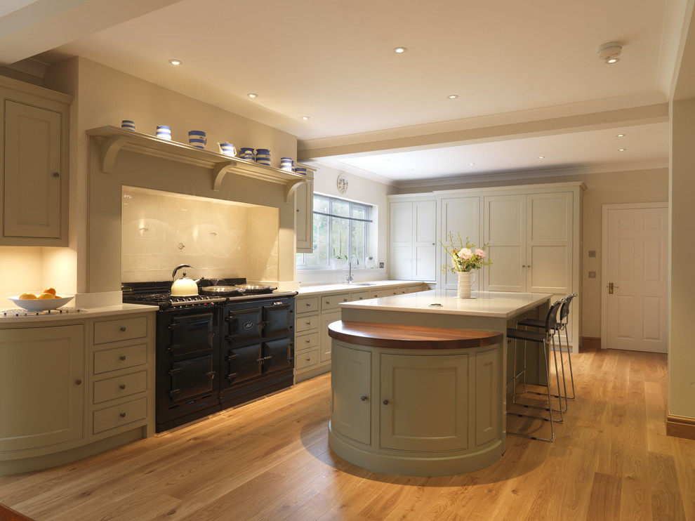 Design ideas for a large traditional u-shaped kitchen/diner in Hampshire with an integrated sink, recessed-panel cabinets, white cabinets, engineered stone countertops, beige splashback, ceramic splashback, black appliances, light hardwood flooring and an island.