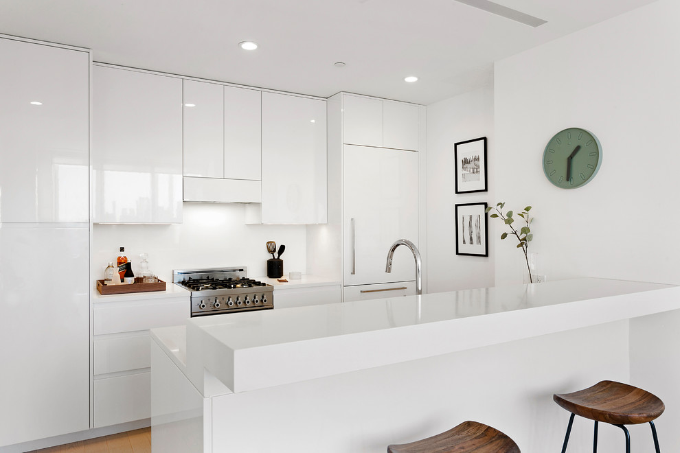 Zweizeilige Moderne Wohnküche mit flächenbündigen Schrankfronten, weißen Schränken, Küchenrückwand in Weiß, Elektrogeräten mit Frontblende, braunem Holzboden, Halbinsel, beigem Boden und weißer Arbeitsplatte in New York