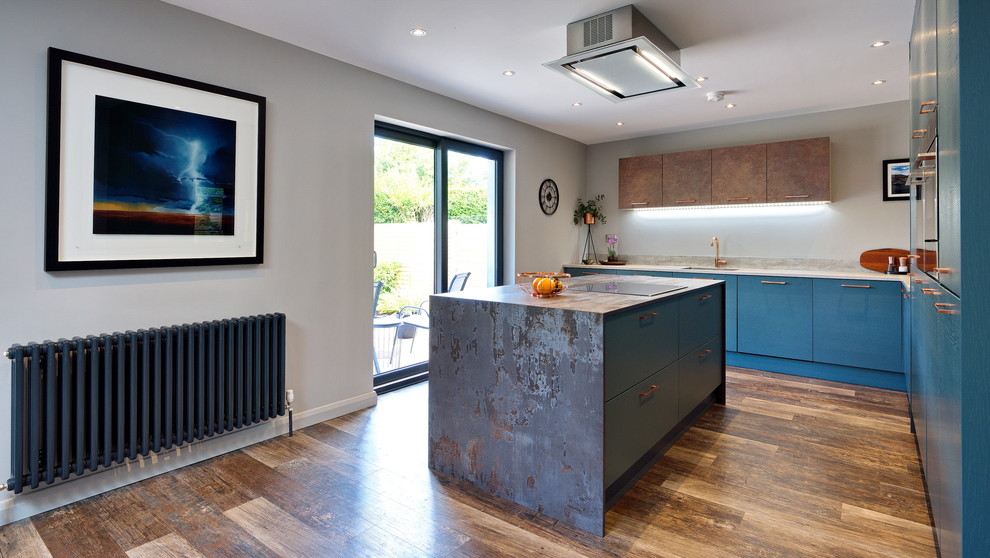 Photo of a medium sized contemporary l-shaped open plan kitchen in Other with a built-in sink, flat-panel cabinets, green cabinets, tile countertops, grey splashback, wood splashback, stainless steel appliances, laminate floors, an island, brown floors and brown worktops.