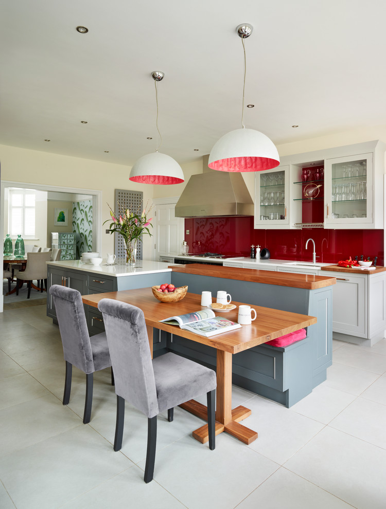 На фото: кухня в стиле неоклассика (современная классика) с обеденным столом, врезной мойкой, стеклянными фасадами, красным фартуком, фартуком из стекла и островом с